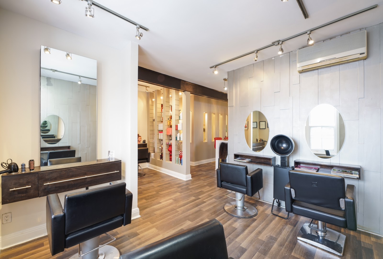 Le salon Aura Lunosa : fauteuils noirs, miroirs ronds et plancher de bois clair